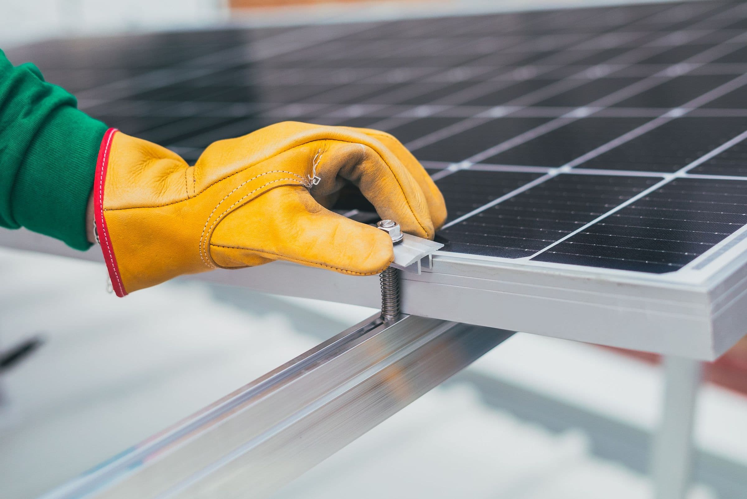 A gloved hand tightening a clamp that fixes a solar panel to its rail