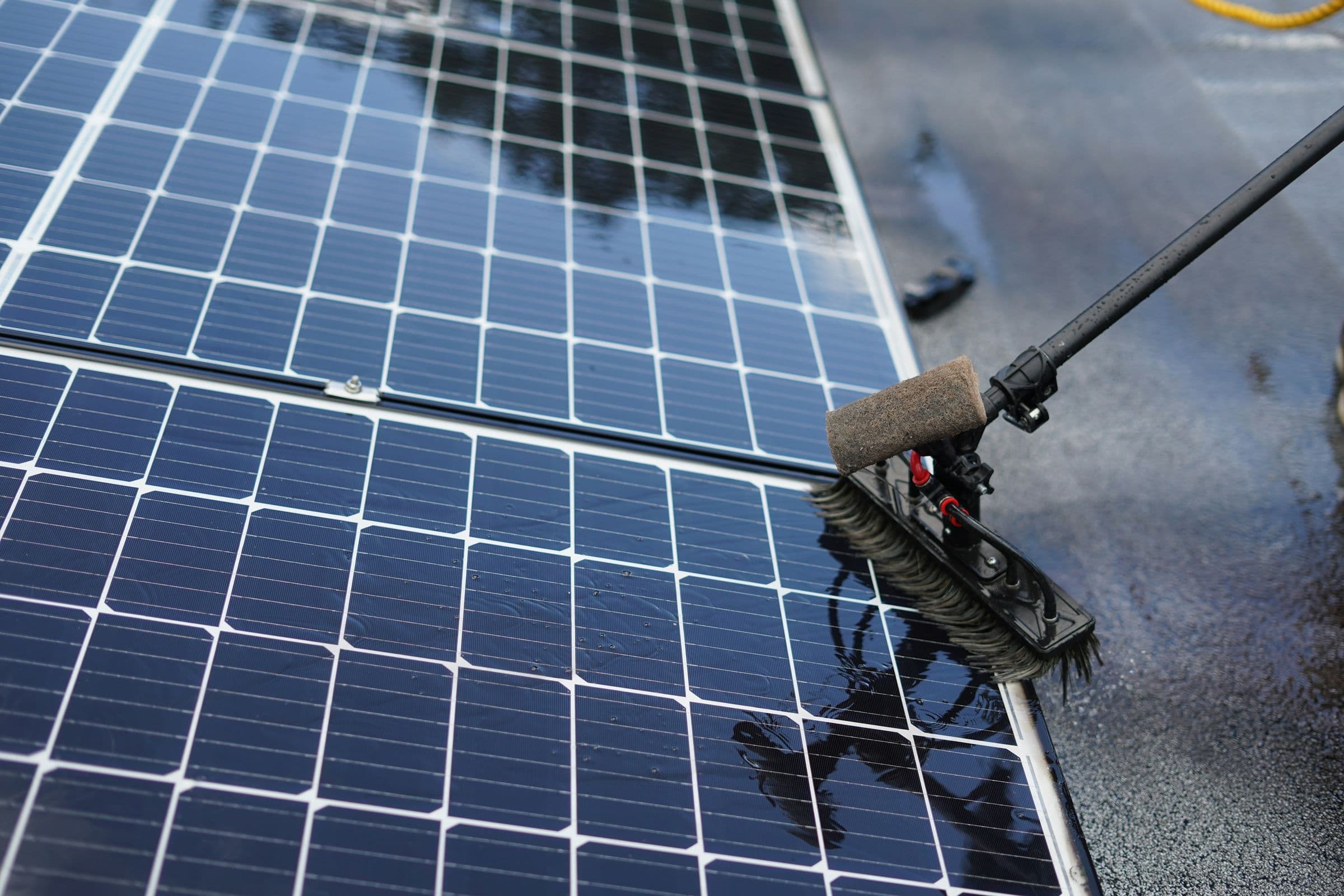 A long-handled brush cleaning a row of wet solar panels