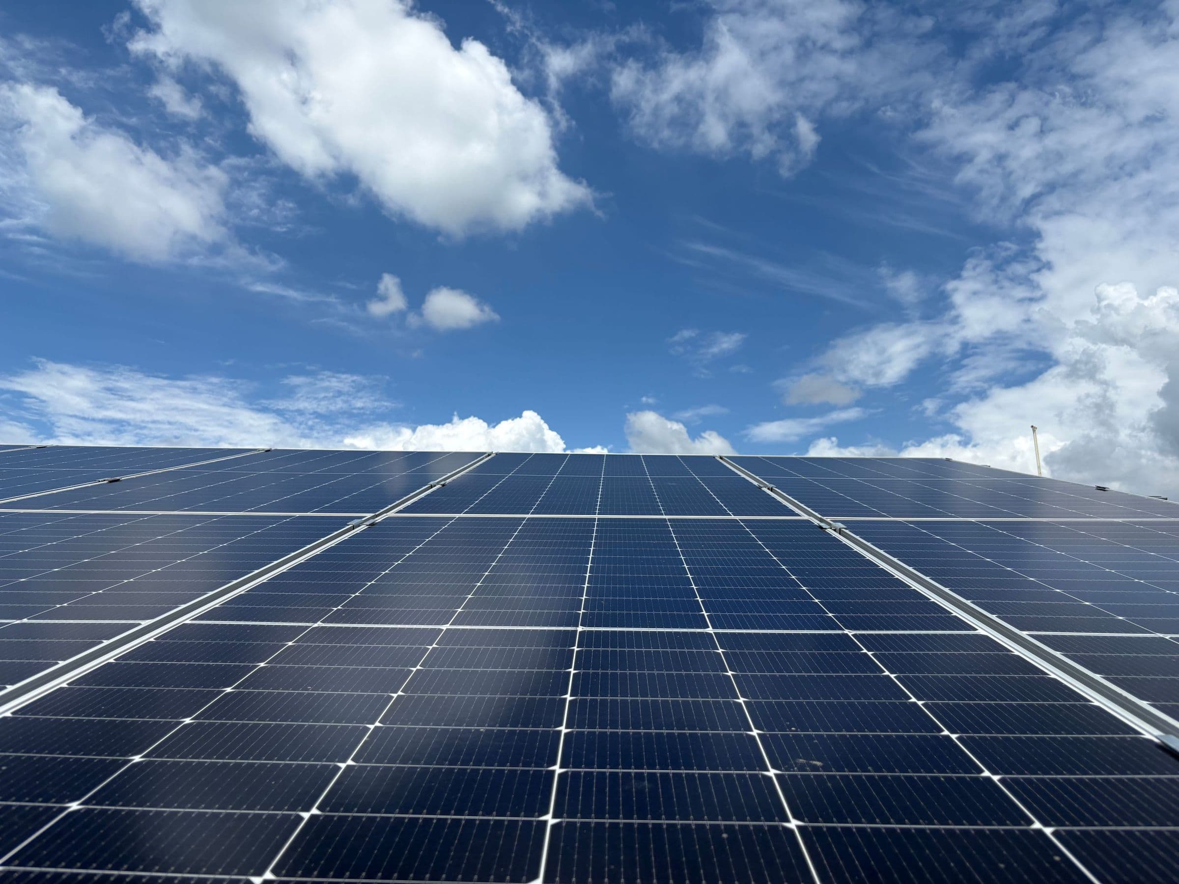 Rows of solar panels on a rooftop under a bright sky with scattered clouds